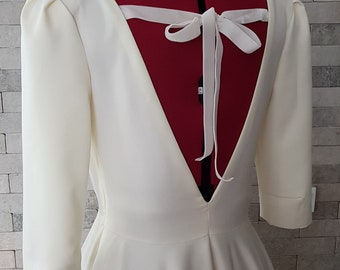 Könnte beinhalten: Ein weißes Kleid mit tiefem V-Ausschnitt und einer weißen Schleife aus Satin. Das Kleid hat 3/4-Ärmel und ein tailliertes Oberteil.