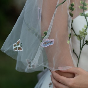 May include: A white dress with a sheer overlay featuring embroidered butterflies and floral details.