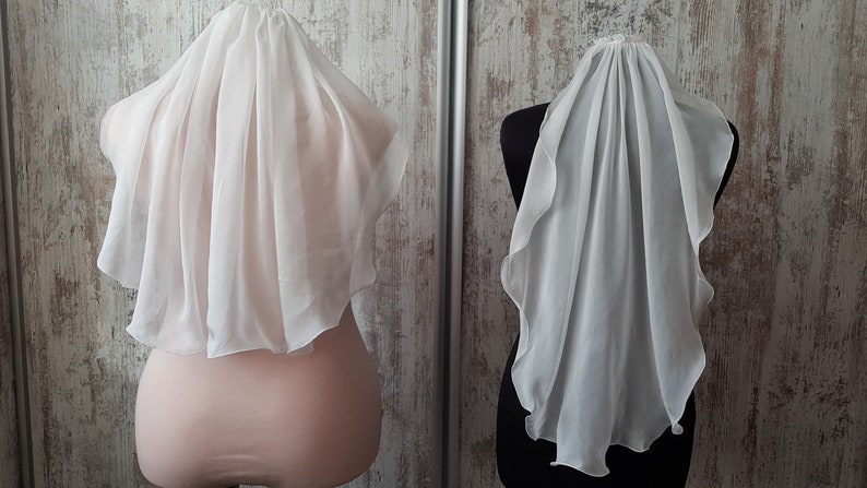Op de afbeelding: Twee witte bruids sluiers tentoongesteld op mannequins. De sluiers zijn gemaakt van zachte, doorschijnende stof en hebben een delicaat, vloeiende ontwerp.