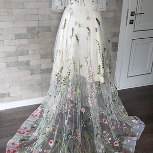 May include: A white tulle gown with a floral embroidery design. The gown has a V-neckline and short sleeves. The skirt is full and flowing, with a train.