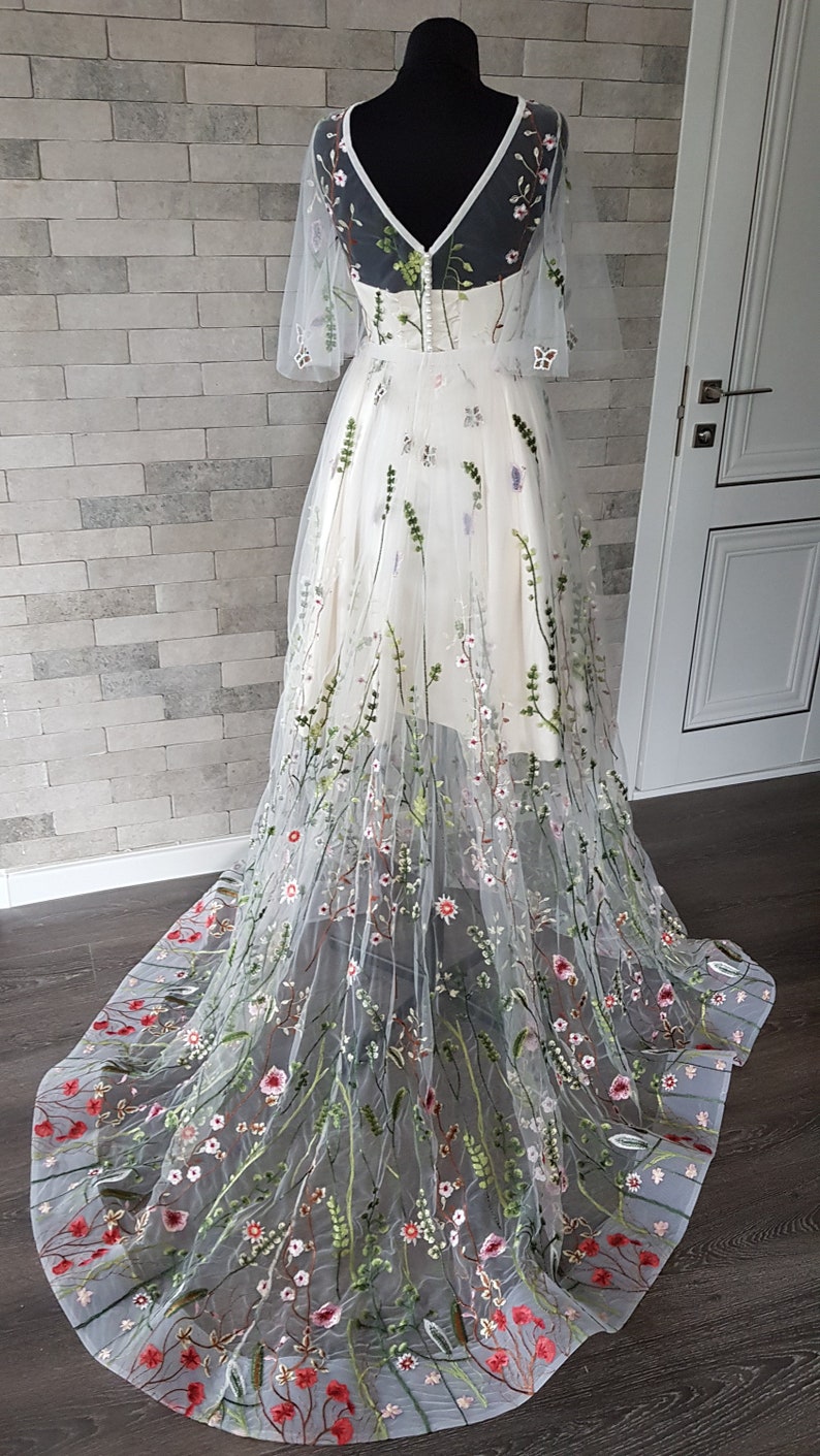 May include: A white tulle gown with a floral embroidery design. The gown has a V-neckline and short sleeves. The skirt is full and flowing, with a train.