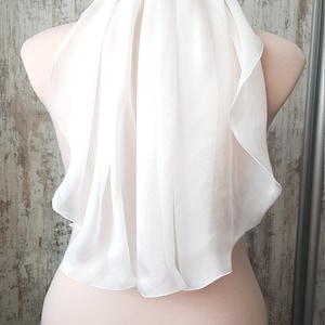 Op de afbeelding: Een witte tule bruids sluier met een gegolfde rand. De sluier is gedrapeerd over het hoofd en de schouders van een mannequin.