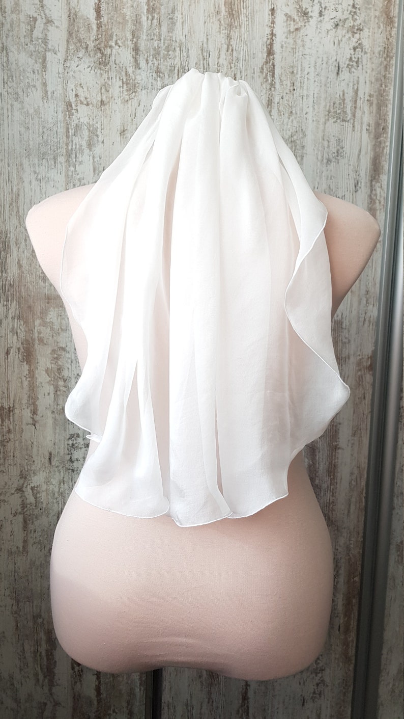 Op de afbeelding: Een witte tule bruids sluier met een gegolfde rand. De sluier is gedrapeerd over het hoofd en de schouders van een mannequin.