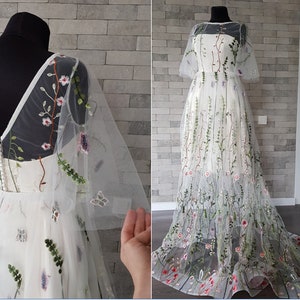 May include: A white tulle wedding dress with floral embroidery. The dress has a V-neckline, short sleeves, and a full skirt. The embroidery features flowers, leaves, and butterflies in shades of pink, green, and blue.