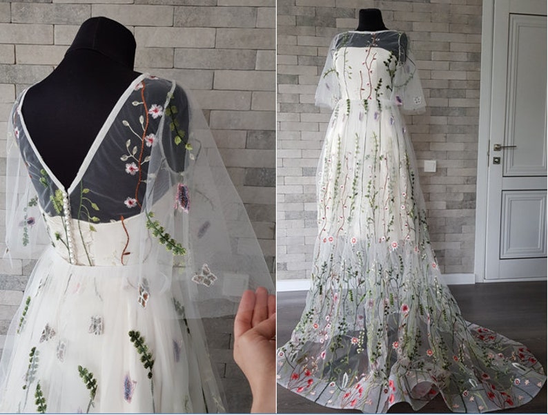 May include: A white tulle wedding dress with floral embroidery. The dress has a V-neckline, short sleeves, and a full skirt. The embroidery features flowers, leaves, and butterflies in shades of pink, green, and blue.