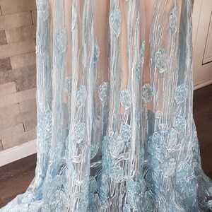 May include: A light blue tulle maxi dress features delicate floral embroidery. The embroidery is in a lighter shade of blue, creating a subtle contrast against the dress's base color. The dress is made of a sheer fabric, allowing for a glimpse of the underlayer. The skirt is full and flows gracefully, showcasing the intricate detailing of the embroidery. The dress is perfect for special occasions, offering a touch of elegance and sophistication.