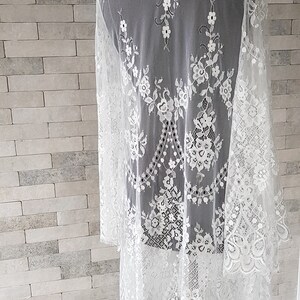 May include: White lace kimono-style cardigan with long sleeves and a scalloped hem. The lace features a floral pattern.  The lightweight, sheer fabric drapes elegantly. This delicate piece is perfect for adding a touch of romance to any outfit.