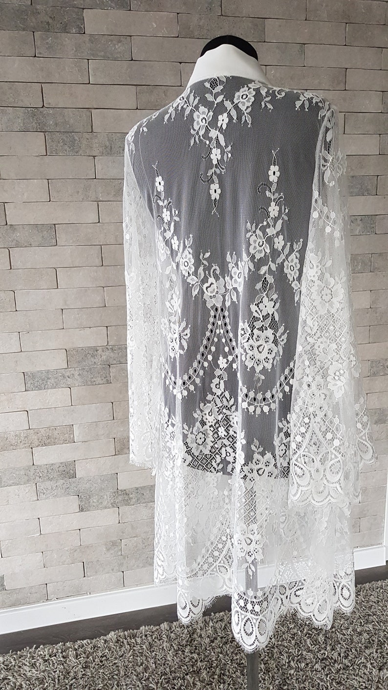 May include: White lace kimono-style cardigan with long sleeves and a scalloped hem. The lace features a floral pattern.  The lightweight, sheer fabric drapes elegantly. This delicate piece is perfect for adding a touch of romance to any outfit.