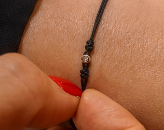 May include: A simple black string bracelet with a small, clear gemstone accent.