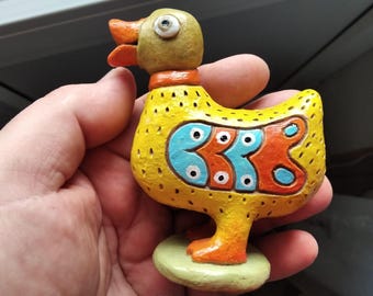 Pequeña escultura de arcilla de un pato amarillo para decoración de mesa o maceta.