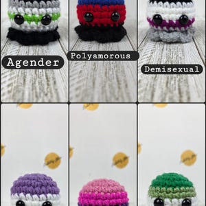 May include: A collection of six crocheted plushies, each with a unique color scheme and design. The plushies are labeled with terms like "Agender," "Polyamorous," and "Demisexual." Each has black button eyes and a ruffled base, with the text labels below.