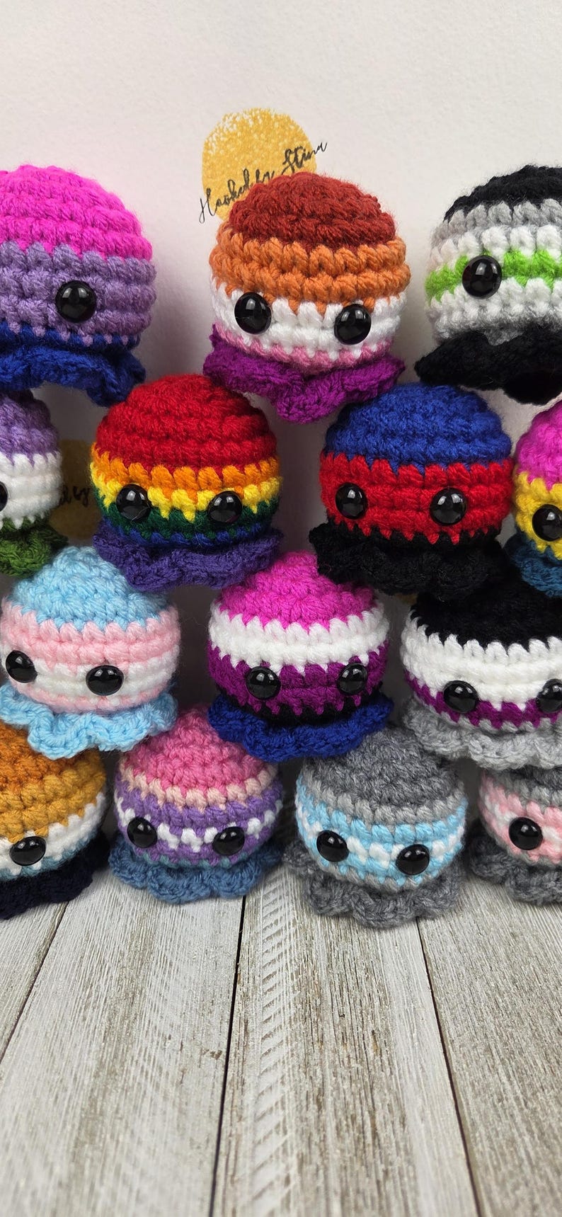 May include: A collection of handmade crochet octopus plushies in various colors, each representing different LGBTQ+ pride flags. The plushies have black button eyes and are arranged on a light wooden surface.