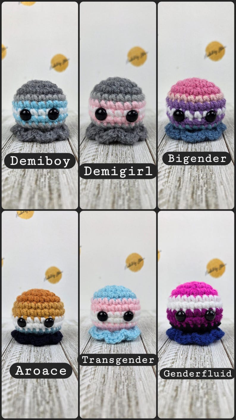 May include: A collection of six crocheted octopus plushies, each with a unique color scheme representing different gender identities. The plushies have large black eyes and a ruffled base. Text labels identify each octopus as Demiboy, Demigirl, Bigender, Aroace, Transgender, and Genderfluid.