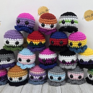 May include: A collection of colorful, crocheted octopus plushies. Each octopus features a different color scheme, including rainbow, pink, blue, and yellow, with black button eyes. The plushies are arranged in a pyramid shape.
