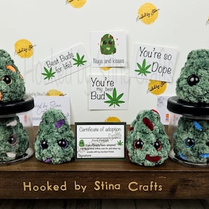 May include: Six green plush weed bud toys in glass jars with various colorful details. The jars are on a wooden shelf with the text "Hooked by Stina Crafts".  The toys are accompanied by four cards with various messages, including "Best Buds for life!" and "You're so Dope".