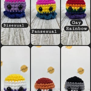May include: Crocheted octopus plushies in various pride flag colors, including bisexual, pansexual, gay rainbow, nonbinary, lesbian, and asexual. Each plush has black button eyes and a ruffled base, with the flag's colors on the body.