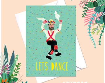 May include: Greeting card with a whimsical illustration of a dancing figure in traditional attire. The card has a teal background with confetti and the words "LET'S DANCE" in yellow. A white envelope is behind the card.