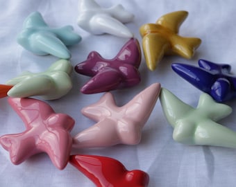 May include: A collection of ten ceramic bird figurines in various colors, including blue, green, pink, red, purple, and yellow. The birds are all in a flying position and have a glossy finish.