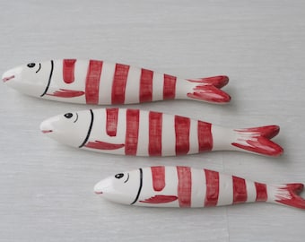 May include: Three ceramic fish figurines with red and white stripes. The fish are different sizes and are arranged in a row from largest to smallest.