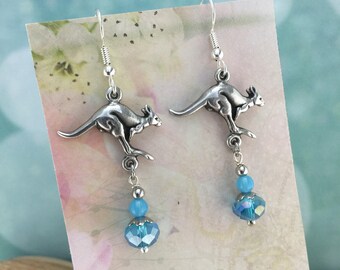 May include: Silver dangle earrings featuring a kangaroo charm and a light blue crystal bead.