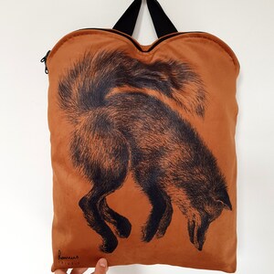 May include: A brown tote bag with a black fox illustration. The bag has a black handle and zipper. The fox is depicted with detailed black fur, and the bag is hanging against a white background.