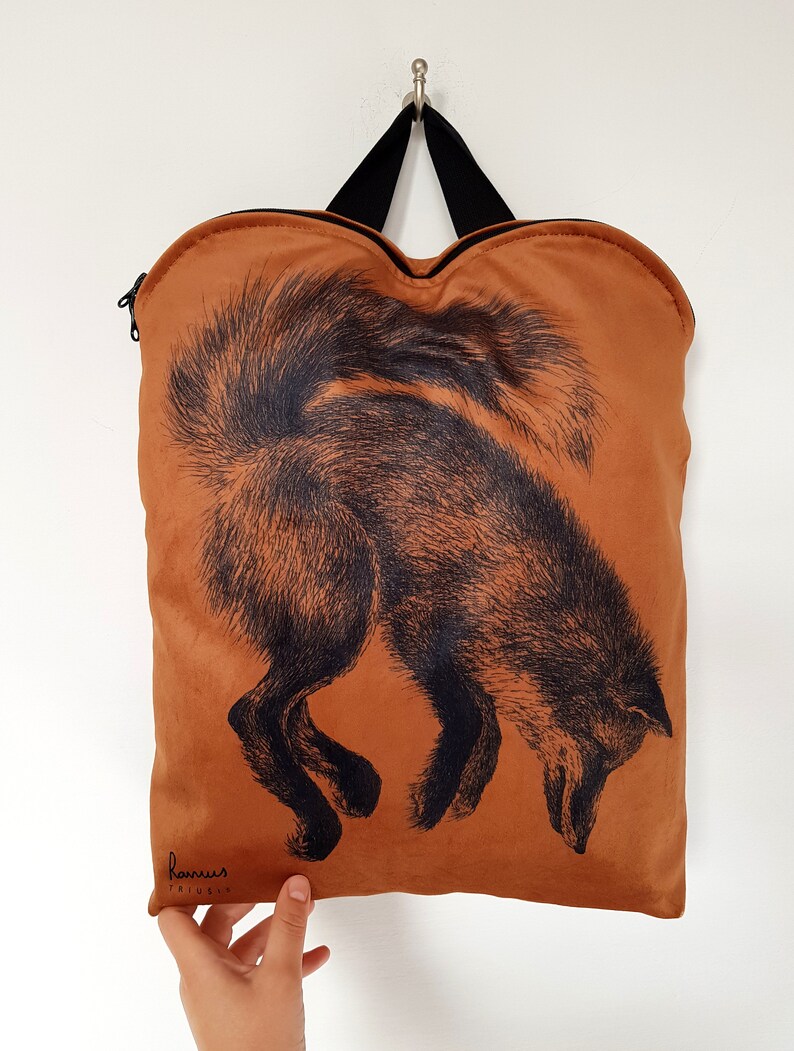 May include: A brown tote bag with a black fox illustration. The bag has a black handle and zipper. The fox is depicted with detailed black fur, and the bag is hanging against a white background.