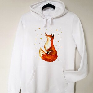 Puede incluir: Sudadera con capucha blanca con un zorro rojo mirando hacia arriba a las estrellas doradas impresas en la parte delantera.