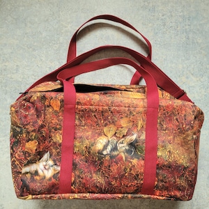 Op de afbeelding: Een rechthoekige duffeltas met een herfstthema met katten tussen herfstbladeren in tinten rood, oranje en goud. De tas heeft rode handvatten en een schouderriem.