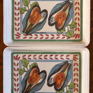May include: Two rectangular white ceramic serving trays. Each tray features a colorful illustration of two open mussels with orange interiors, blue shells, and green accents. The trays have a green and red border.