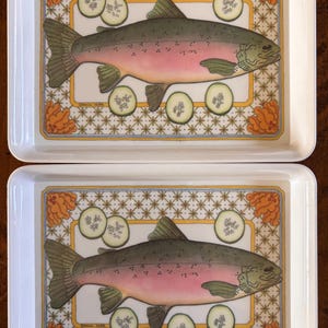 May include: Two rectangular serving trays with a fish and cucumber design. The fish is pink and green, with cucumber slices and floral accents. The trays have a white border and a decorative pattern.