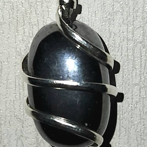 May include: A black gemstone pendant wrapped in silver wire. The pendant is oval shaped and has a smooth, polished surface.