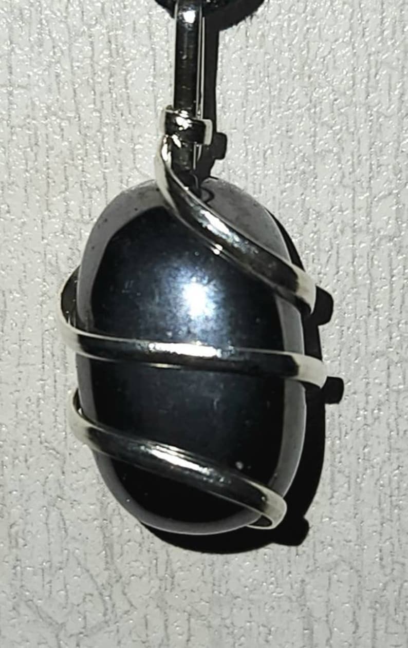 May include: A black gemstone pendant wrapped in silver wire. The pendant is oval shaped and has a smooth, polished surface.