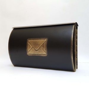 May include: Black metal mailbox with a gold envelope design. The mailbox has a rounded front and a rectangular shape.