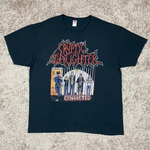 Puede incluir: Camiseta negra con el nombre de la banda "Cryptic Slaughter" en letras rojas y blancas. La camiseta presenta un gráfico de una escena de prisión con la palabra "Convicted" debajo. La camiseta tiene cuello redondo y mangas cortas.