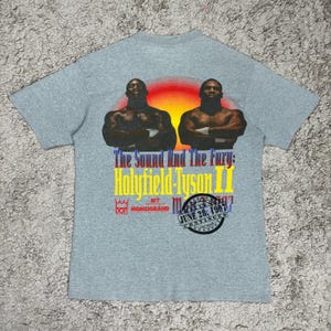 May include: A grey t-shirt with a graphic of two boxers, the text "The Sound And The Fury: Holyfield-Tyson II", and event details. The design includes a sunset backdrop and the date June 28, 1997.