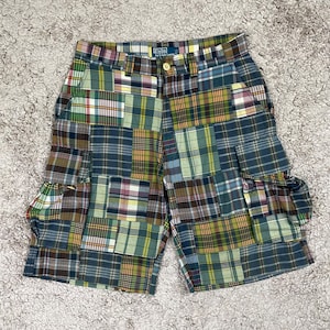 May include: Multi-colored plaid shorts with cargo pockets. The shorts feature a patchwork design with various plaid patterns in shades of blue, green, yellow, and brown. The shorts have a button closure and a Polo by Ralph Lauren label.