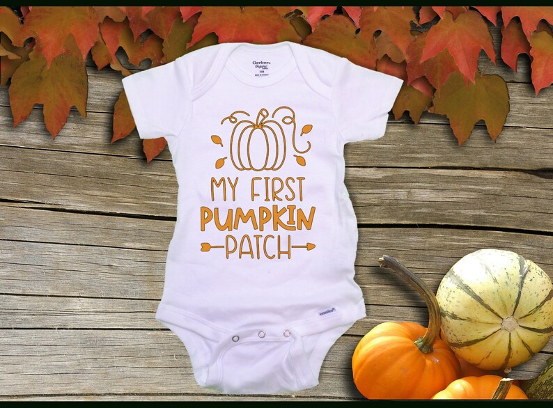 Pode incluir: Macac&atilde;o branco para beb&ecirc; com uma ab&oacute;bora laranja e o texto "My First Pumpkin Patch" em laranja.