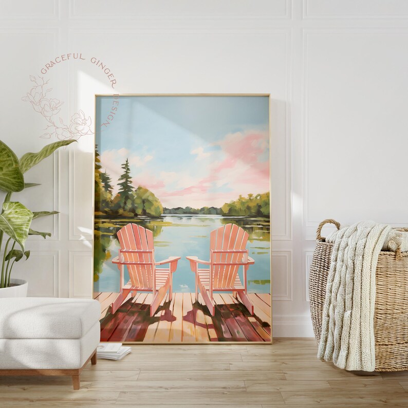 May include: A framed painting depicts two coral-colored Adirondack chairs on a wooden dock overlooking a serene lake scene. The sky is a blend of blue and pink hues, with trees lining the distant shore. The artwork evokes a sense of tranquility.