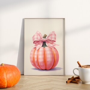 Puede incluir: Una impresi&oacute;n enmarcada de una calabaza rosa con un lazo de cuadros. La calabaza es de color rosa claro con l&iacute;neas verticales, y el lazo presenta un patr&oacute;n de cuadros rosa a juego. La impresi&oacute;n est&aacute; apoyada contra una pared blanca.