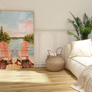 May include: A framed art print depicts two orange Adirondack chairs on a wooden dock overlooking a lake. The artwork features a serene landscape with trees, water, and a colorful sky. The scene evokes a sense of relaxation and leisure.