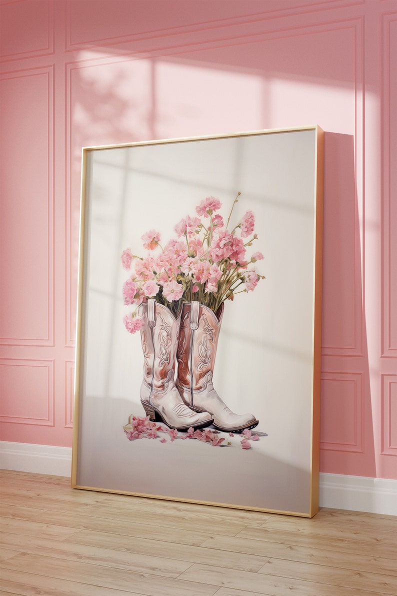 May include: A framed print of a pair of white cowboy boots with pink carnations in the tops. The boots are on a white background with a few pink petals scattered around them.