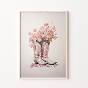 May include: A pair of white cowboy boots with pink flowers in the tops. The boots are on a white background with pink flower petals scattered around them.