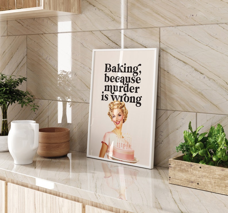 Peut inclure: Une impression encadr&eacute;e blanche avec le texte "Baking, because murder is wrong." Une femme aux cheveux blonds tient un g&acirc;teau rose avec des bougies.