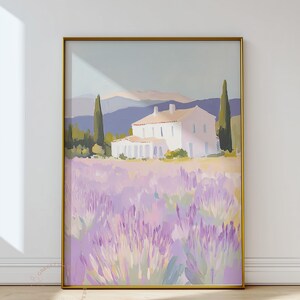 Large framed painting of a lavender field landscape with a cream-colored villa in the distance. The bold golden frame contrasts with the delicate hues of lilac, sage, and rose in the artwork.