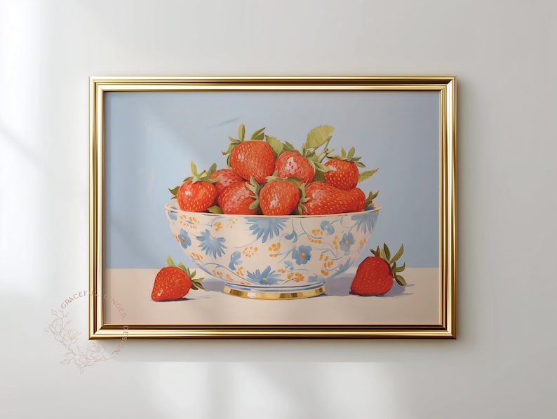 Framed painting of ripe strawberries piled in a white ceramic bowl decorated with blue and yellow flowers. A few strawberries rest beside the bowl on a flat surface. The background is soft blue, and the gold frame adds a refined touch to the still-life composition.