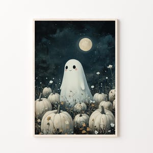 May include: A framed print featuring a whimsical illustration of a friendly ghost in a field of pumpkins under a full moon. The artwork has a soft, painterly style with a dark blue night sky and white pumpkins.