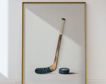 May include: A framed print featuring a hockey stick and puck. The hockey stick is brown with a white grip and black blade. The puck is dark blue. The artwork is set against a white background and framed in gold.