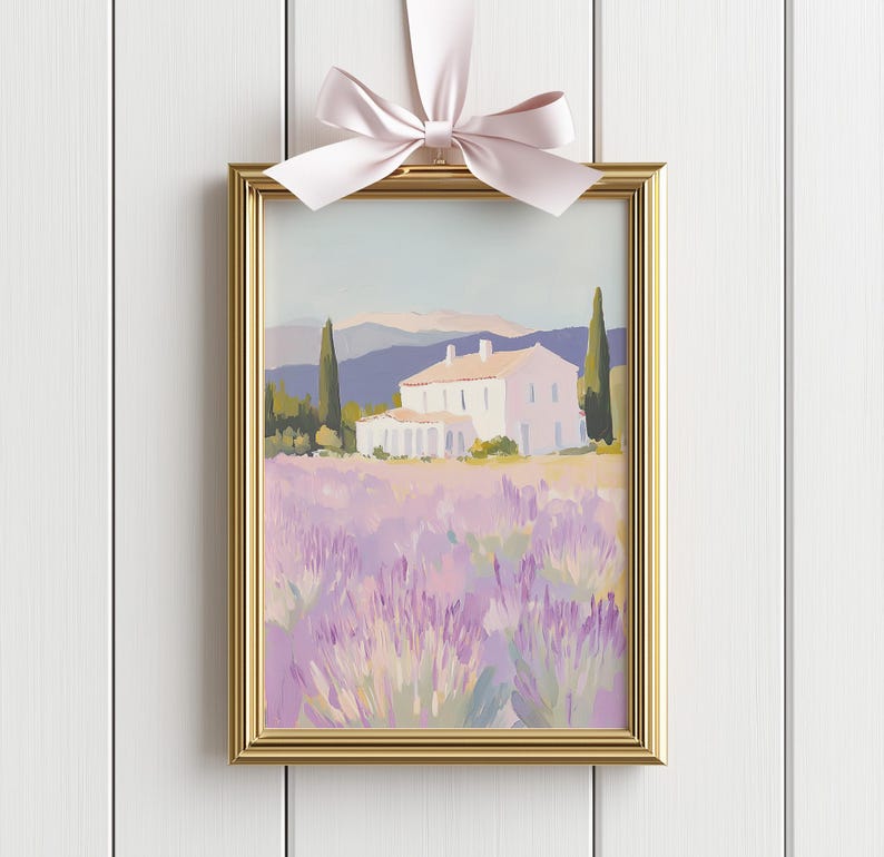 Framed painting of a countryside villa and lavender field, adorned with a soft pink ribbon bow. Displayed against white vertical paneling, the piece blends romantic charm with timeless elegance.
