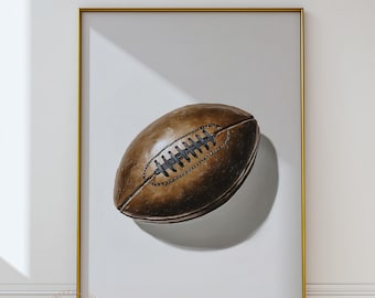 May include: A framed print featuring a detailed illustration of a brown football. The football has black stitching and is set against a white background. The artwork is framed in a gold-colored frame, adding a touch of elegance.