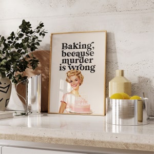 Peut inclure: Une affiche encadr&eacute;e avec une illustration r&eacute;tro d'une femme tenant un g&acirc;teau rose. Le texte sur l'affiche dit "Baking, because murder is wrong."